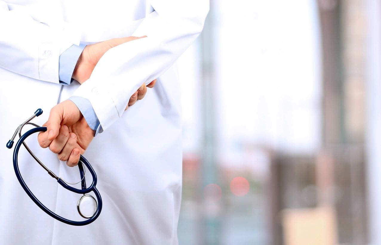 A person in white lab coat holding a pair of stethoscopes.